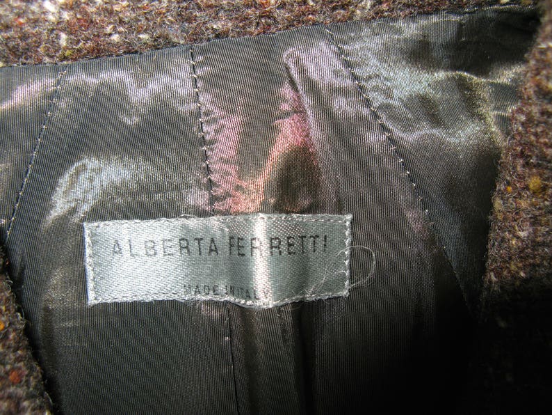 May include: A close-up of a brown wool jacket with a black satin lining. The label reads "Alberta Ferretti! Made in Italy."