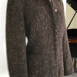 May include: A brown tweed jacket with a button closure and a white seam down the front.