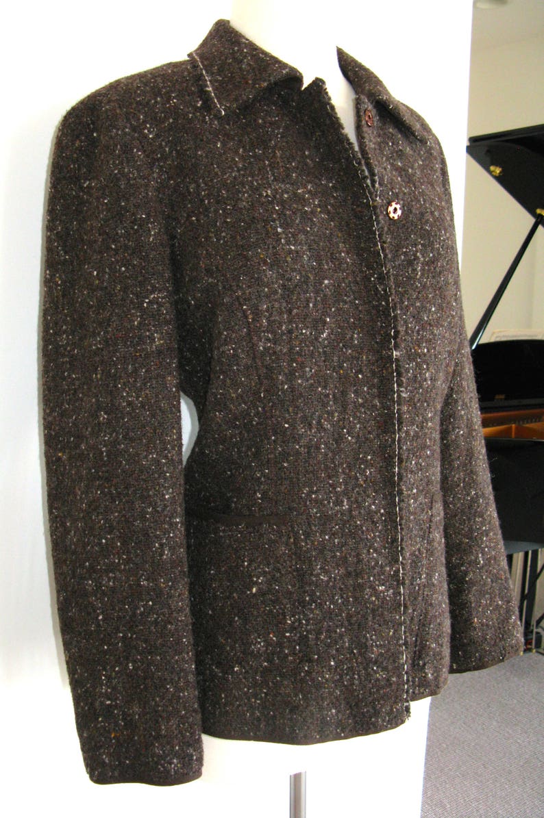 May include: A brown tweed jacket with a button closure and a white seam down the front.