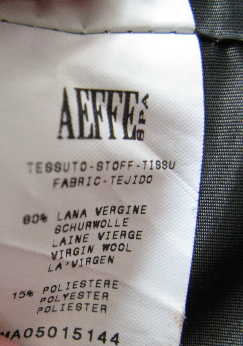 May include: A white fabric label with black text that reads "AEFFE" and "TESSUTO-STOFF-TISSU FABRIC-TEJIDO". The label lists the fabric composition as 80% virgin wool and 15% polyester. The label also includes the number "A05015144".