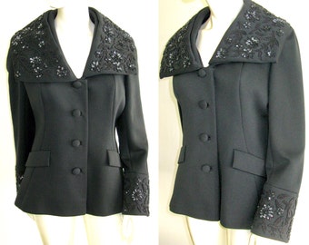 May include: A black blazer with a wide, beaded collar and beaded cuffs. The blazer has a v-neck and a button closure.