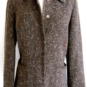 May include: A brown tweed blazer with a single button closure and two pockets. The blazer has a subtle speckled pattern and a white stitching detail.