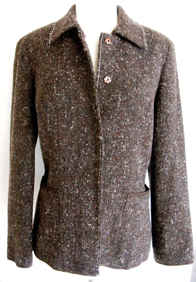 May include: A brown tweed blazer with a single button closure and two pockets. The blazer has a subtle speckled pattern and a white stitching detail.