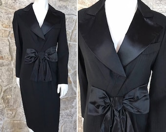 May include: A black dress with a satin bow at the waist. The dress has a pinstripe pattern and a satin collar.