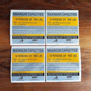 May include: Four white and yellow stickers with black text. Each sticker reads "MAXIMUM CAPACITIES" and lists capacity details: 14 persons or 902 kg, 2540 lbs, persons, motor, gear, and 115 H.P. motor.