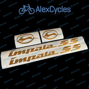 Puede incluir: Calcomanías Impala SS y logotipo Impala doradas sobre un respaldo blanco. Las calcomanías son para vehículos y presentan un diseño estilizado de gacela saltando. El fondo es negro con el logotipo de AlexCycles.