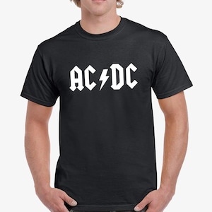 Op de afbeelding: Zwart T-shirt met het witte "AC/DC" logo en bliksemgrafiek. Het ontwerp is in vette blokletters. Het T-shirt heeft een ronde hals.