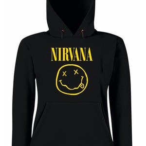 Può includere: Felpa con cappuccio nera con la scritta "NIRVANA" in giallo sopra una faccina sorridente gialla. La felpa ha una tasca frontale e un cappuccio con coulisse. Il design è un'icona musicale classica.