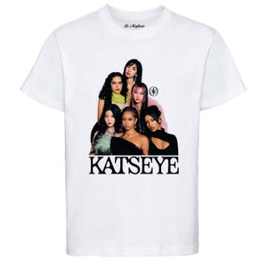May include: White crew neck t-shirt featuring a group of six women. The word "KATSEYE" is printed in large, black, bold letters at the bottom. The shirt has a small logo on the upper back. The women are in various outfits.