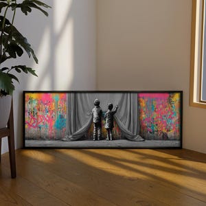 以下が含まれることがあります： 2人の子供が灰色のカーテンの前に立っている、額入りのアートプリント。 カーテンは開かれ、ピンク、黄色、青、オレンジ色のスプラッシュが施されたカラフルなグラフィティウォールが現れます。 アートワークは木製の床に展示されています。