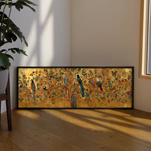 Può includere: Un'opera d'arte incorniciata con uno sfondo dorato raffigurante un albero con uccelli colorati, farfalle e fiori. L'opera d'arte è in una cornice nera ed è esposta su un pavimento in legno. È un pezzo decorativo.