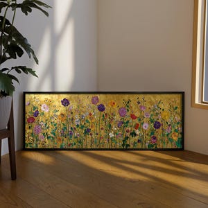 Könnte beinhalten: Ein rechteckiges gerahmtes Kunstwerk mit einer lebendigen Blumenwiese vor goldenem Hintergrund. Die Blumen sind in den Farbtönen Lila, Rot, Gelb und Weiß gehalten. Der Rahmen ist schwarz, und das Kunstwerk wird auf einem Holzboden präsentiert.