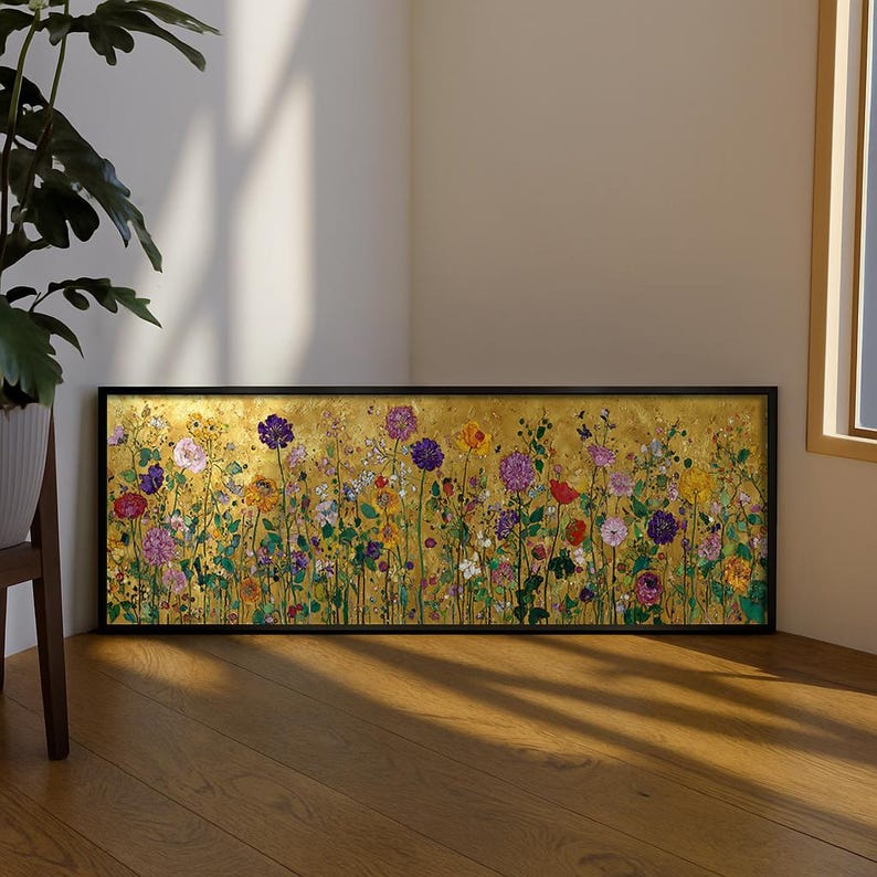 Puede incluir: Una pieza de arte mural rectangular en un marco negro que presenta una pintura horizontal de un prado de flores silvestres. La obra muestra una vibrante variedad de flores moradas, rosas, amarillas y rojas sobre un fondo dorado texturizado.
