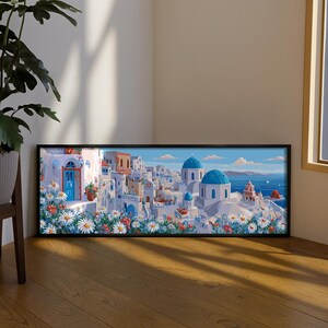 May include: A framed art print depicting a coastal village with white buildings, blue domes, and a blue sea. The artwork features a vibrant color palette with white, blue, and red accents, and is surrounded by white and red flowers.