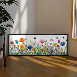 May include: A framed watercolor print featuring a vibrant meadow of colorful wildflowers in shades of pink, orange, yellow, blue, and purple. Several bees are depicted flying above the flowers. The frame is black.