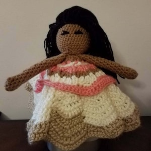 Puede incluir: Mu&ntilde;eca de crochet con piel marr&oacute;n, cabello negro y un vestido rosa y blanco. La mu&ntilde;eca lleva un vestido de crochet con un patr&oacute;n rosa y blanco.