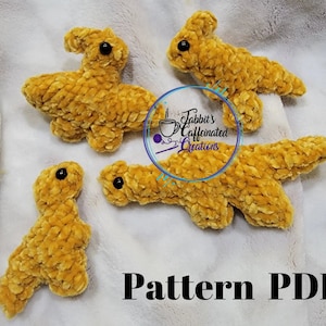 May include: Four crocheted dinosaur plushies in a mustard yellow color. The plushies are made with a fuzzy yarn and have black eyes. The plushies are on a white fuzzy surface. The text "Pattern PDF" is at the bottom of the image.