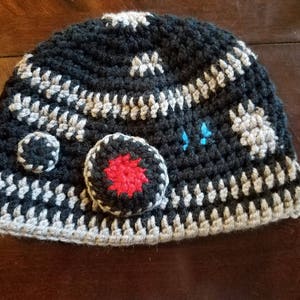 May include: A black and gray crocheted hat with a red and blue star design. The hat is made of yarn and has a textured surface.