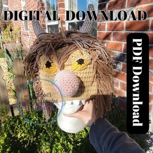 Op de afbeelding: Gehaakte muts met een bruine en bruine vachttextuur, een roze neus en gele ogen. De muts is monsterachtig met hoorns. De tekst "DIGITAL DOWNLOAD" en "PDF Download" is zichtbaar in de afbeelding.