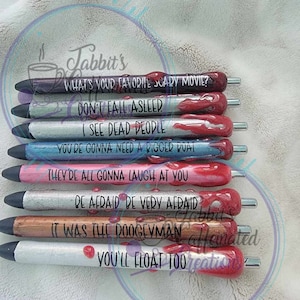 May include: A set of eight silver pens with black and red paint, each with a different quote from a horror movie. The quotes include "What's your favorite scary movie?", "Don't fall asleep", "I see dead people", "You're gonna need a bigger boat", "They're all gonna laugh at you", "Be afraid be very afraid", "It was the doogeyman", and "You'll float too".