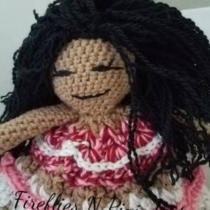 Puede incluir: Mu&ntilde;eca de crochet con cabello negro largo, vistiendo un vestido rosa y blanco con un dise&ntilde;o de crochet. La mu&ntilde;eca tiene una tez morena y sonr&iacute;e. El texto "Fireflies N Pixiedust" es visible en la parte inferior de la imagen.
