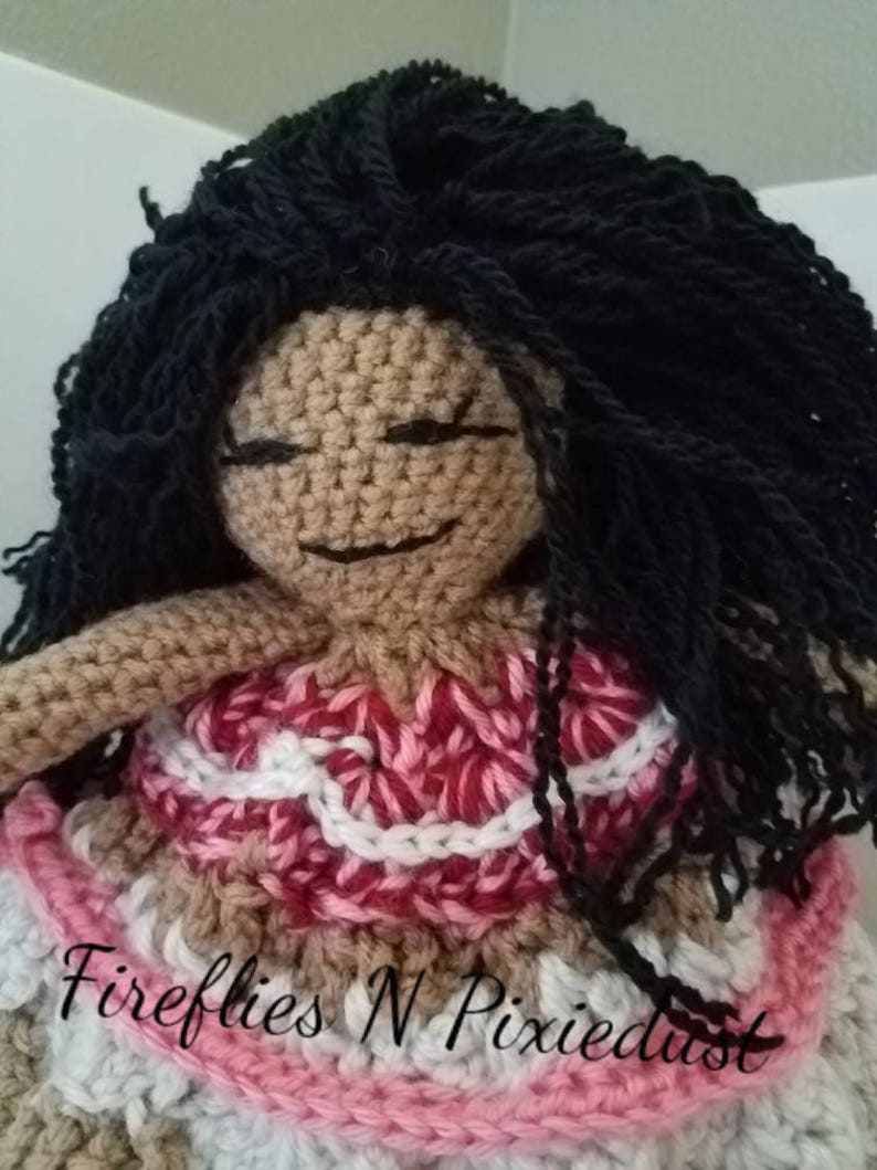 Puede incluir: Mu&ntilde;eca de crochet con cabello negro largo, vistiendo un vestido rosa y blanco con un dise&ntilde;o de crochet. La mu&ntilde;eca tiene una tez morena y sonr&iacute;e. El texto "Fireflies N Pixiedust" es visible en la parte inferior de la imagen.