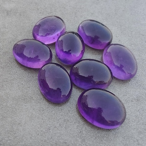May include: Seven polished, oval-shaped amethyst gemstones with a deep purple hue. Each stone features a smooth, rounded surface with a reflective, glossy finish, showcasing the natural translucent quality and rich violet color of the quartz.