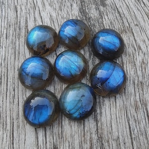 May include: Seven round, polished labradorite cabochons arranged in a cluster. Each stone features a smooth, domed surface with a dark gray base color and a vibrant, iridescent blue flash that shifts across the surface of the polished gemstones.