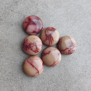May include: Six circular cabochons with a smooth, polished finish. Each piece features a light tan base color with distinct, irregular dark red veining patterns that resemble marble or natural stone textures across the rounded surfaces.
