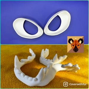 May include: Two white, oval-shaped eye pieces and a white jaw set are displayed against a blue and yellow background. A small illustration of a wild dog is in the corner. The items appear to be props or parts of a costume.