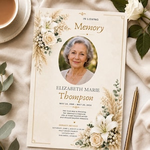 May include: A memorial card featuring a portrait of a woman, adorned with floral accents. The card displays the words "In Loving Memory", the name Elizabeth Marie Thompson, dates, and a touching message. A gold pen is placed nearby.