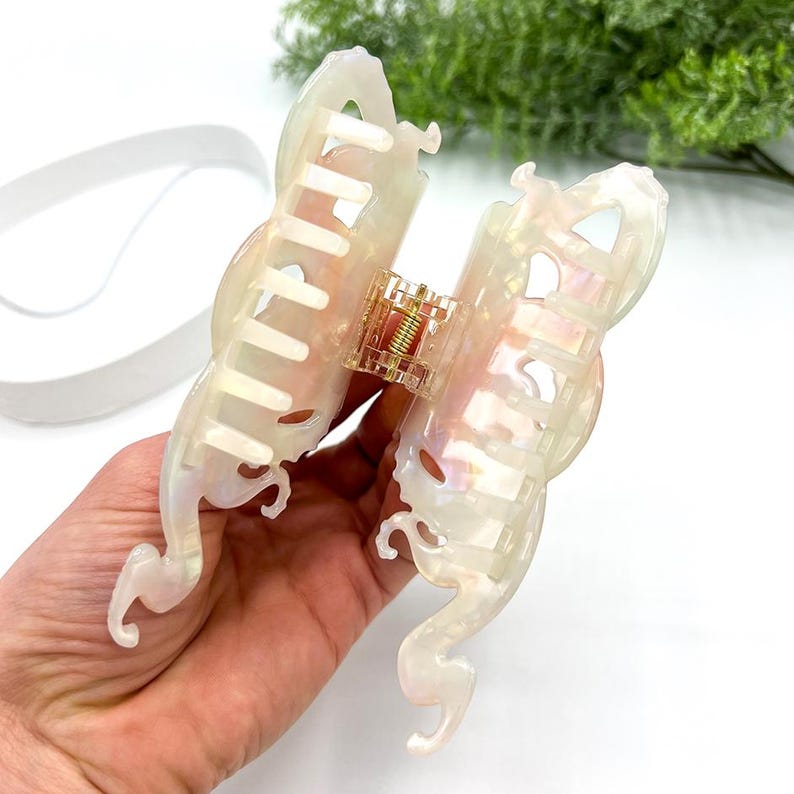 Puede incluir: Pinza para el pelo iridiscente con dise&ntilde;o de mariposa. La pinza presenta un acabado nacarado con toques de rosa y dorado. La pinza tiene un mecanismo de resorte dorado y est&aacute; dise&ntilde;ada para sujetar el cabello de forma segura.
