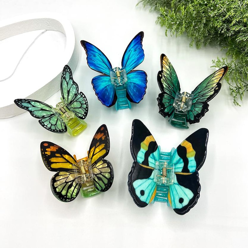 May include: Five butterfly-shaped hair clips in various colors: blue, green, yellow, and black. Each clip features a detailed wing design and a clear plastic clasp. The clips are arranged on a white surface.