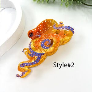 Puede incluir: Tres pinzas para el pelo de resina con forma de pulpo. El estilo #1 es naranja y blanco con detalles morados. El estilo #2 es naranja y amarillo con detalles morados. El estilo #3 es marr&oacute;n y amarillo con detalles morados. El texto "Style #" est&aacute; presente.