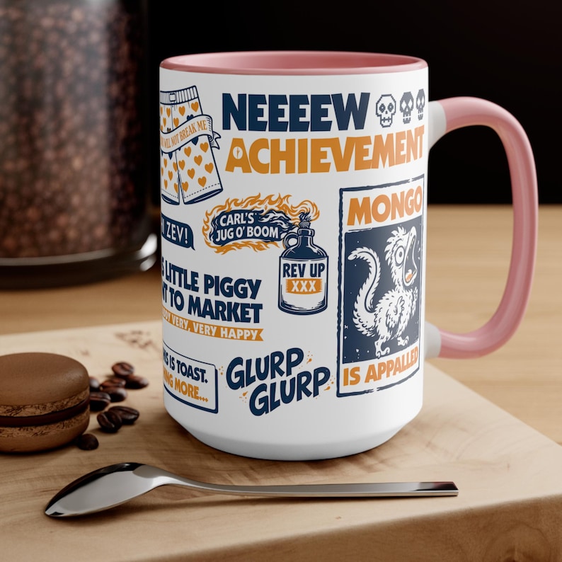 Peut inclure: Mug en céramique blanche avec une anse et un bord intérieur roses. Le mug est recouvert de divers textes et graphiques bleus et orange, dont les mots "Achievement" et "Mongo". Une cuillère et un macaron sont au premier plan.