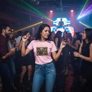 May include: A woman in a pink t-shirt with the text "Apple Bottom Jeans" and a framed image of a painting, paired with blue jeans with floral embroidery, dances in a club. The background features a crowd and colourful lights.