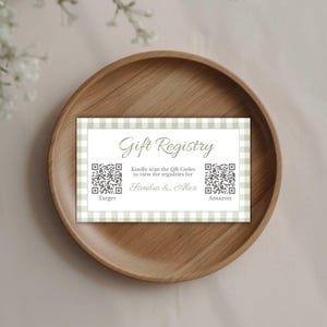 May include: A rectangular gift registry card with a gingham border, featuring the text "Gift Registry" and QR codes for Target and Amazon. The card is placed on a wooden plate.