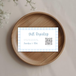 May include: A rectangular gift registry card with a light blue and white gingham border. The text reads Gift Registry, Kindly scan the QR code to view the registry for Sandra & Alex, and includes a QR code with the word Target printed below it.