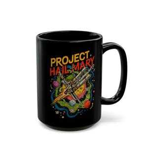 Peut inclure: Mug en céramique noire avec l'inscription "PROJECT HAIL MARY" et une illustration colorée. Le design comprend un vaisseau spatial, des planètes et une esthétique rétro. La tasse a une grande anse.