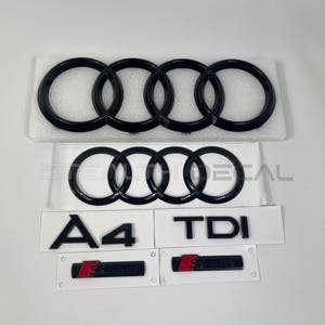 May include: Black Audi car emblems and badges. Includes the Audi four-ring logo, A4 and TDI badges, and two S-Line badges with red accents. The emblems are on a white background.