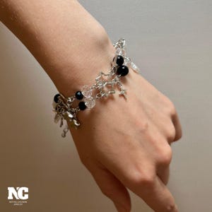 May include: A silver charm bracelet with star and charm accents. The bracelet features black and clear beads. The bracelet is on a person's wrist.