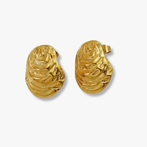 May include: A pair of gold-coloured stud earrings. Each earring has a unique, organic shape with a textured, swirling pattern across the surface. The earrings are displayed against a plain white background.