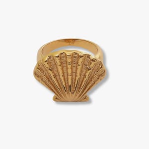 May include: A gold-colored ring featuring a detailed seashell design. The ring has a wide band and a textured, fan-shaped seashell centerpiece. The ring is likely made of metal and is suitable for everyday wear.