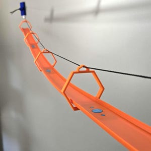 Könnte beinhalten: Eine orangefarbene Spielzeug-Rennstrecke mit schwarzem Faden und blauen Akzenten. Die Strecke ist gebogen und wird von orangefarbenen sechseckigen Rahmen getragen. Oben ist eine blaue und schwarze Komponente angebracht.