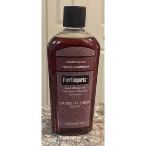 May include: A clear bottle of Pier 1 Imports Asian Spice reed diffuser oil. The bottle has a black cap and a burgundy label with text in English and French. The bottle contains 473 ml of oil.