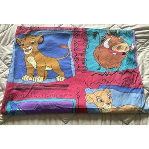 May include: A vibrant pillowcase with characters from The Lion King. The design showcases Simba, Pumbaa, and Nala, set against pink, blue, and purple squares with decorative lines. The pillowcase is likely made of cotton.