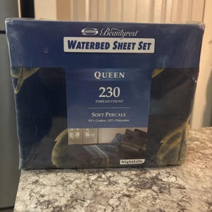 Puede incluir: Un juego de sábanas para cama de agua Beautyrest empaquetado. El paquete azul oscuro presenta el texto "WATERBED SHEET SET", "QUEEN", "230 Thread Count" y "SOFT PERCALE". El juego está hecho de 55% algodón y 45% poliéster. El paquete tiene un diseño Nightfalls.