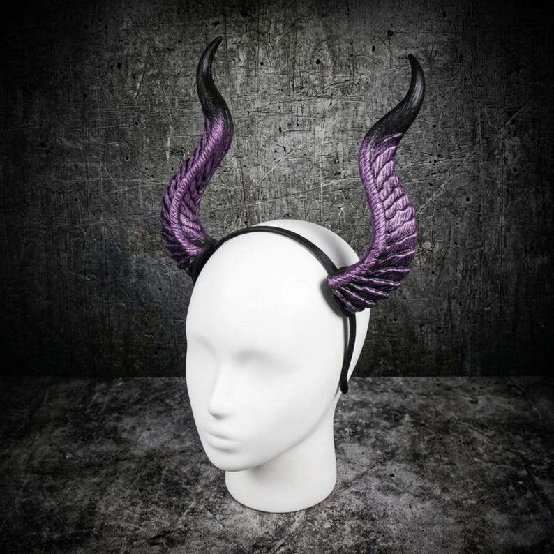 May include: A black headband featuring two large, curved, textured horns that transition from a deep purple at the base to a solid black at the tips. The horns have a ridged, organic surface structure and are mounted on a thin, plain black band.