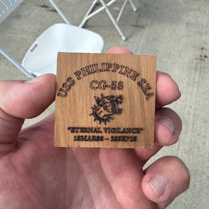 May include: A small, square wooden plaque with engraved text and a graphic. The text reads "USS PHILIPPINE SEA CG-58" and "ETERNAL VIGILANCE" with dates. The graphic is a stylized image of a ship.
