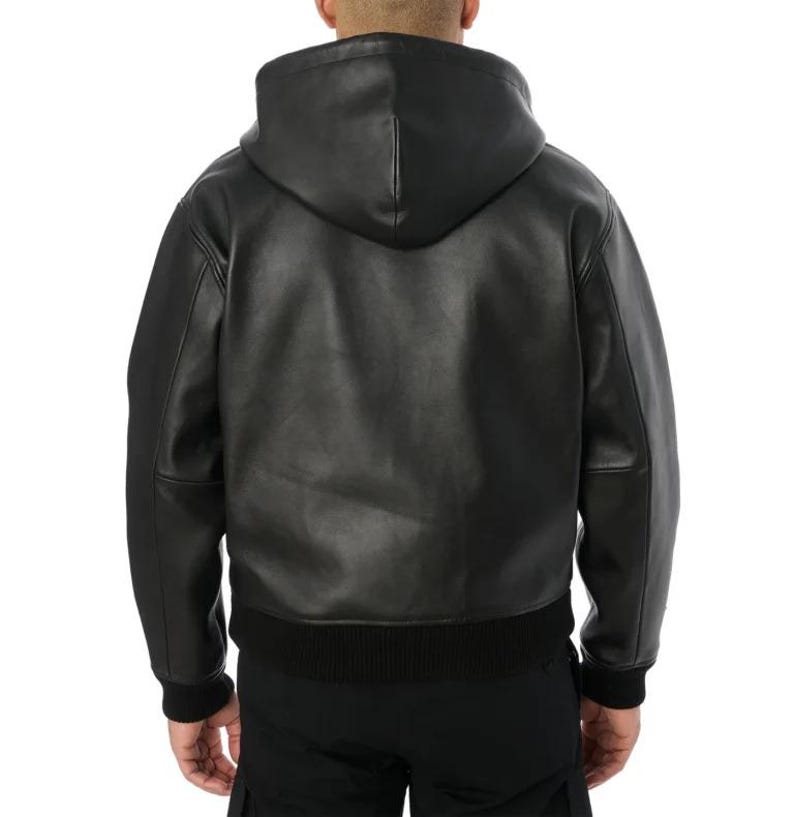 Pu&ograve; includere: Giacca con cappuccio in pelle nera con orlo e polsini a coste. La giacca ha una cerniera a tutta lunghezza e un cappuccio. Vista posteriore che mostra il design della giacca. Stile classico.